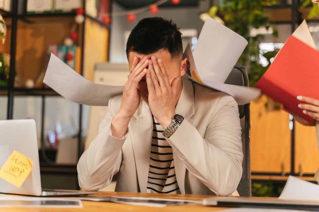 Mann im Büro schlägt die Hände vors Gesicht, Papiere fliegen durch die Luft